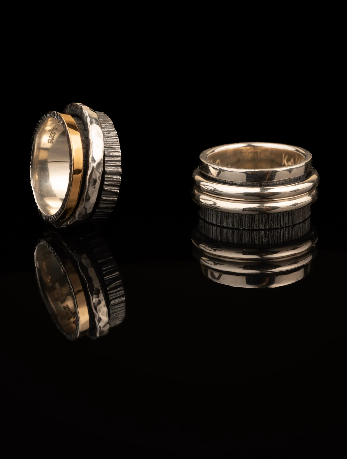 Two K.AND. rings in silver and gold reflected on black