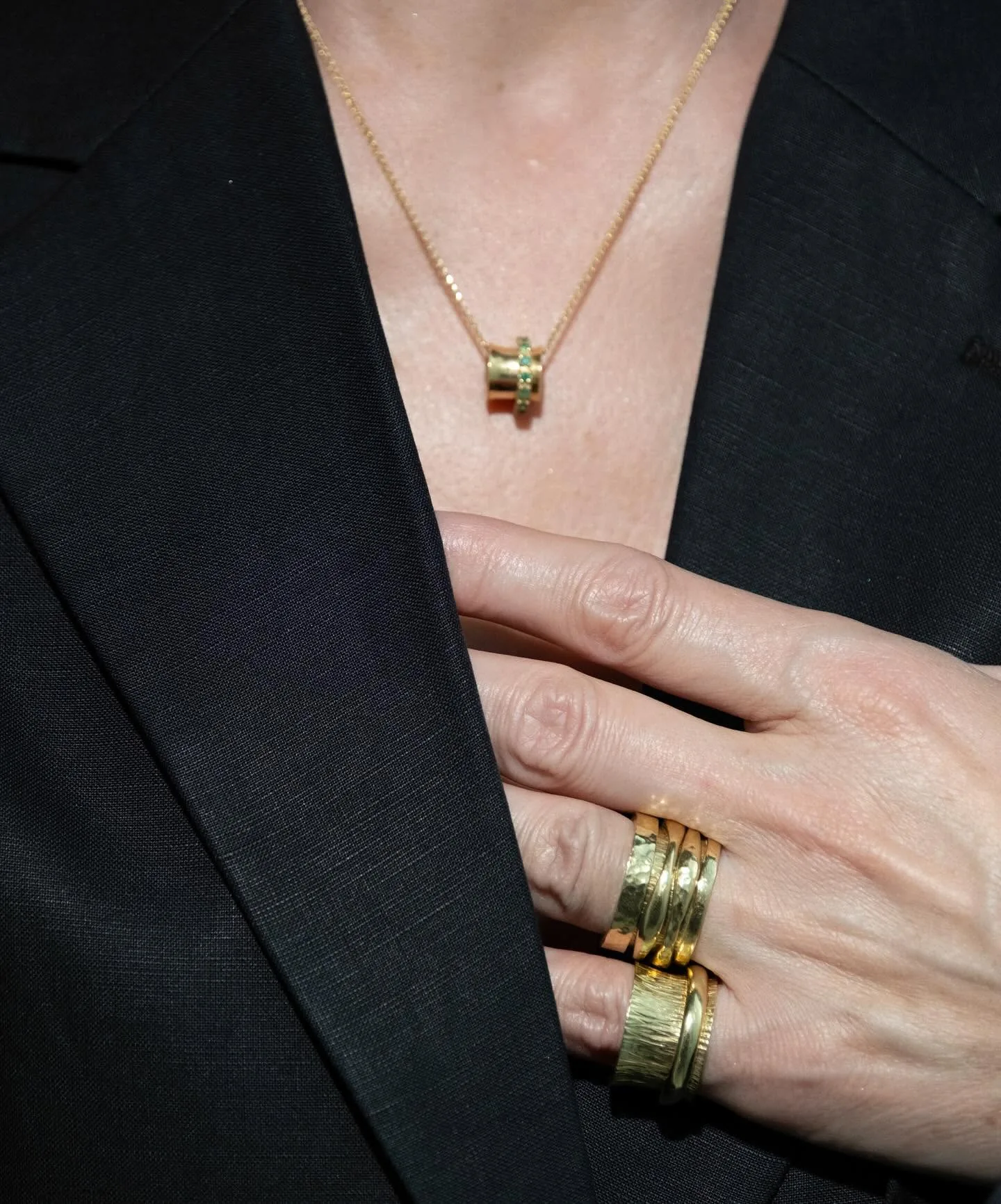 Hand with stacked 18K gold K.AND. rings against a black jacket