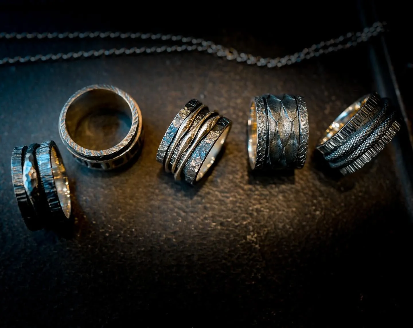 K.AND. rings in silver and gold arranged on a dark surface