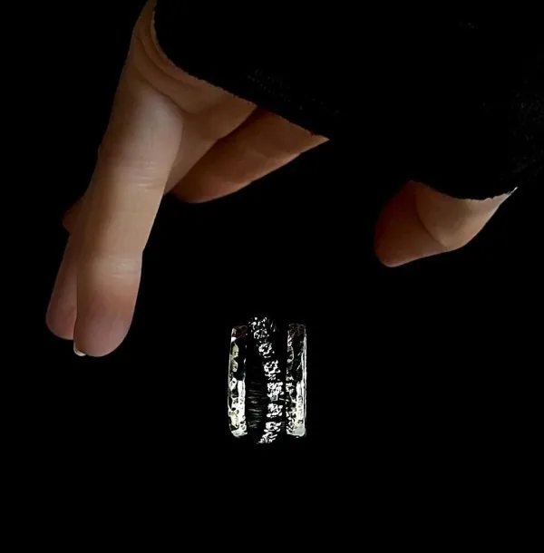 Hand holding a K.AND. ring with clear stones on a black background