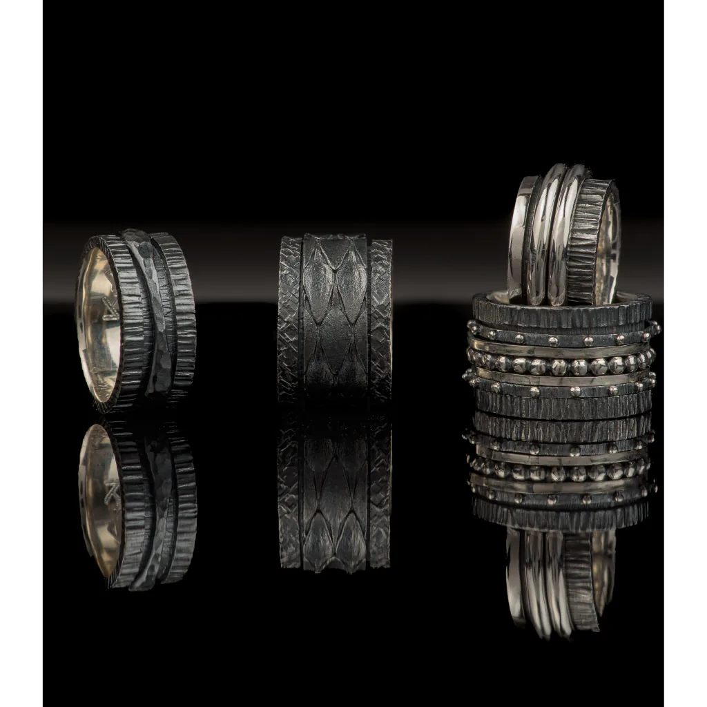 Three oxidised silver K.AND. rings reflected on a black surface
